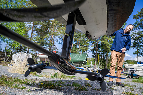 Båtskrov sett underifrån med rigg, motorer, roder och propellrar. I bakgrunden en person.